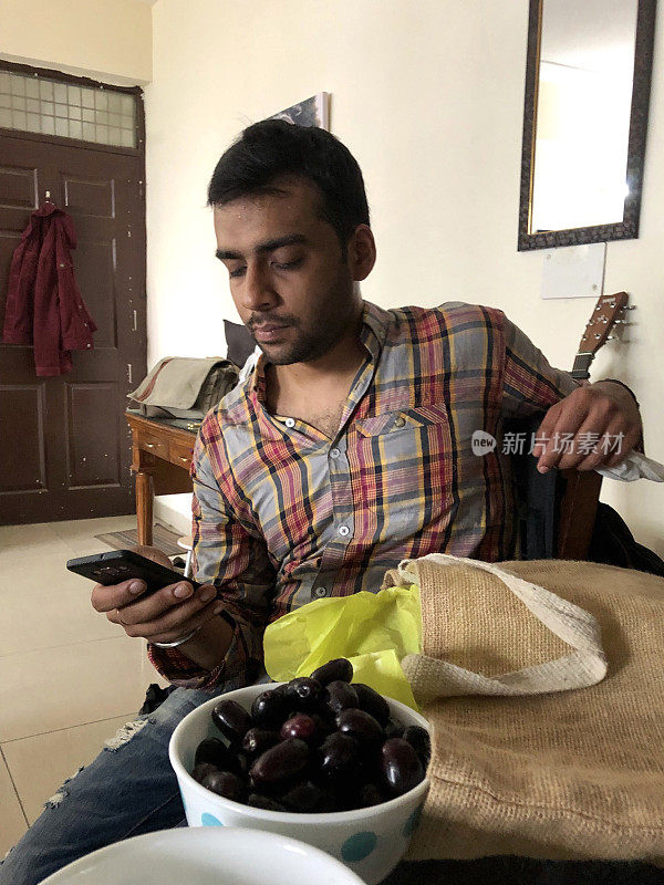 印度男子皱着眉头，在早餐餐桌上专注地看手机短信，穿着格子衬衫/智能手机照片